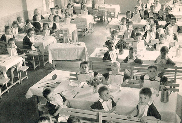 Une vue d'ensemble en noir et blanc d'un réfectoire avec plusieurs enfants attendant leur repas.
